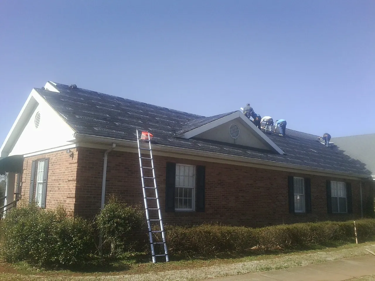 Crew tearing shingles off a brick ranch roof with a ladder set — Emergency Roof Repair work by our crew in Millington